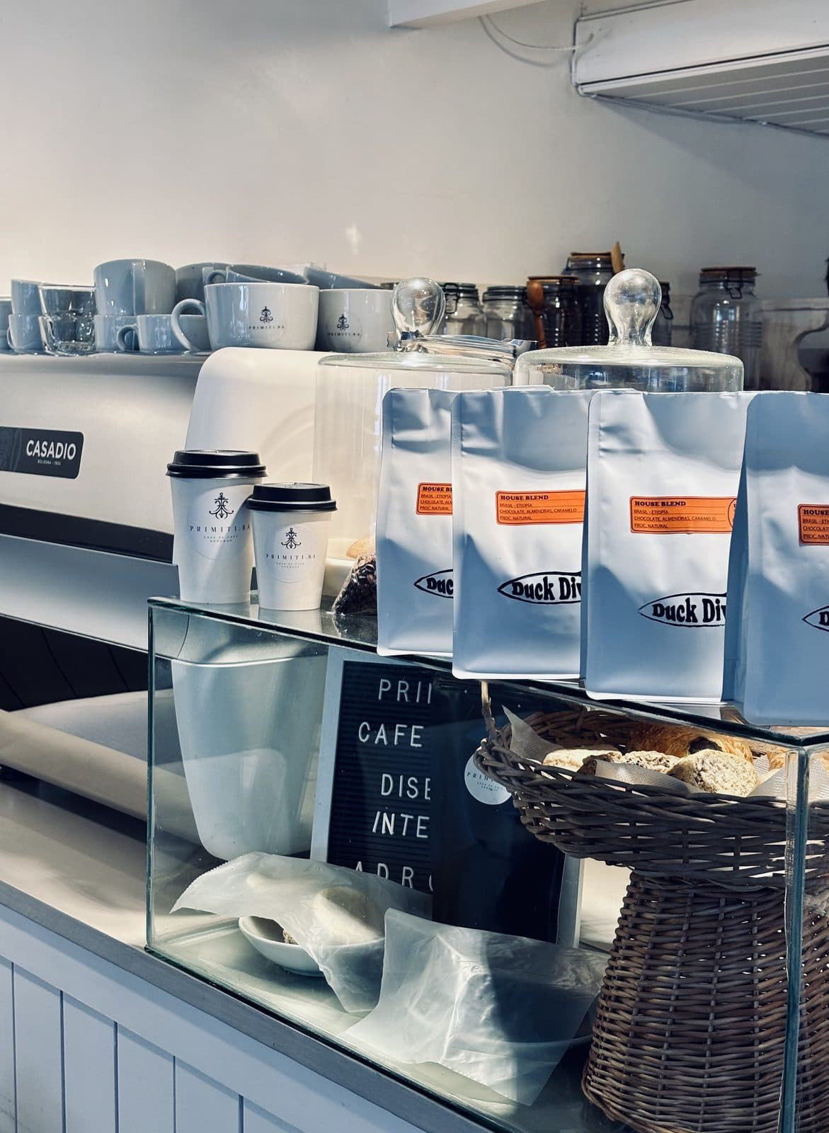 Bolsas de House Blend en la barra de una cafetería, junto a la máquina